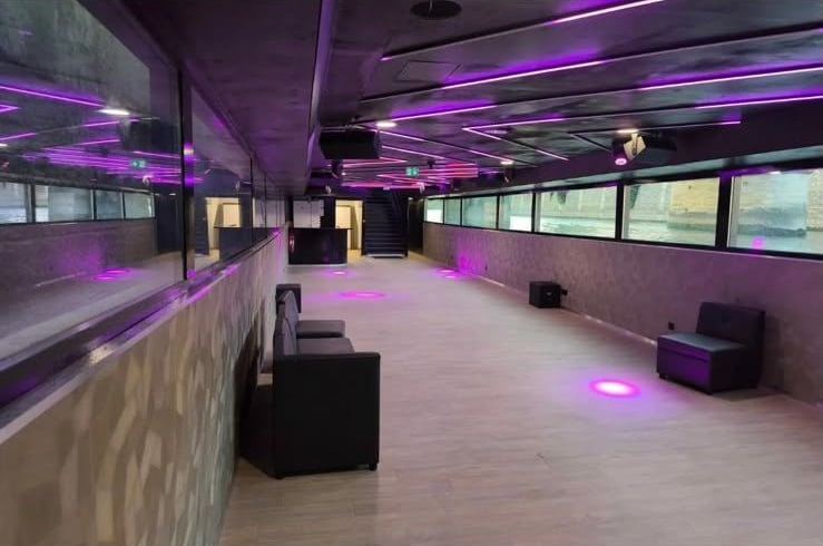 La salle intérieure éclairée en violet, avec banquettes et grandes fenêtres sur la Seine.
